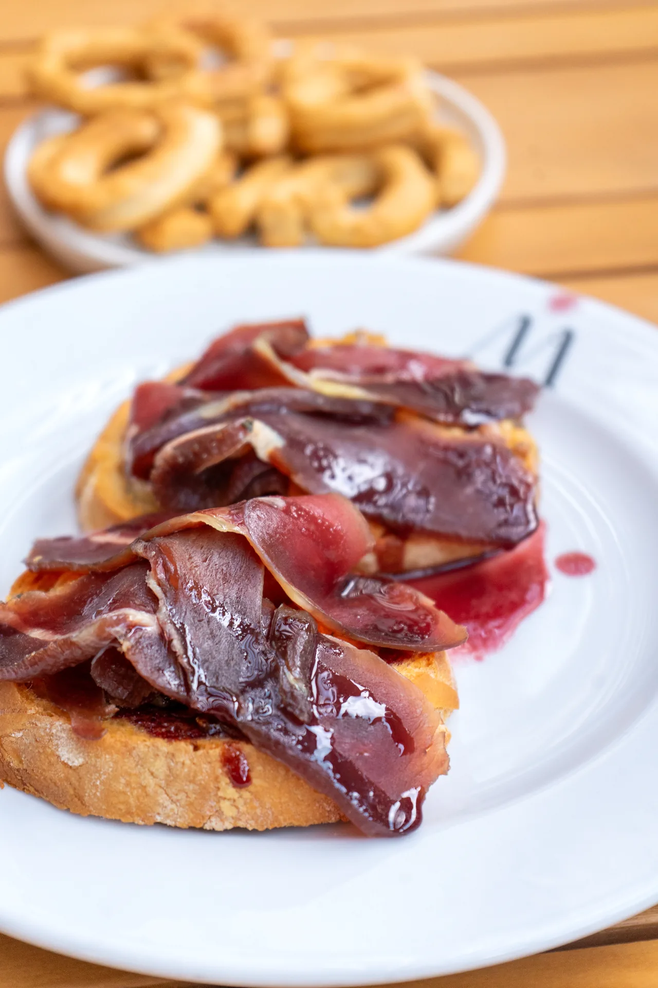 Bruschetta con salume a fette sottili su pane tostato, con taralli sullo sfondo